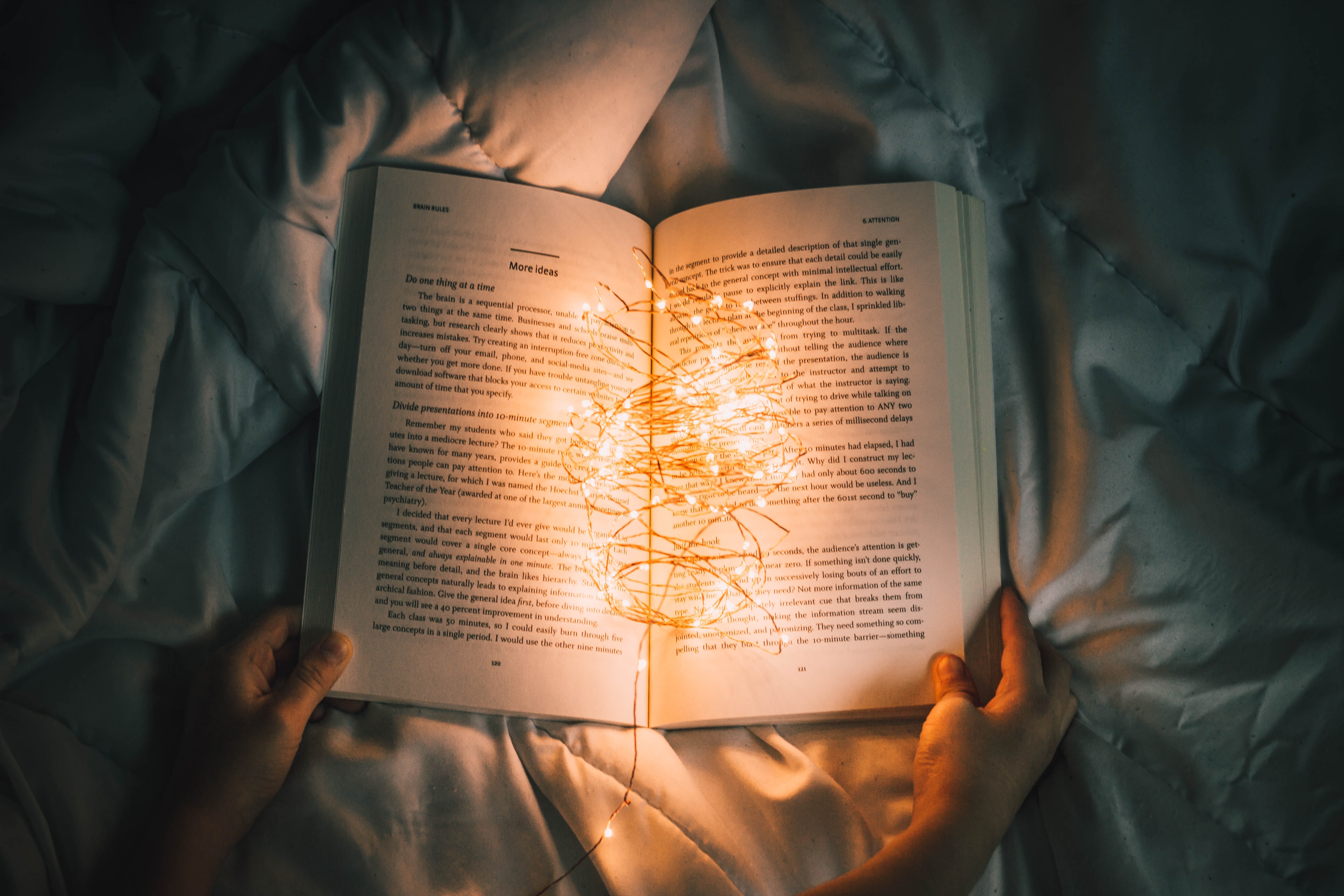 a person sitting on a bed with an open book that has fairy light on it.