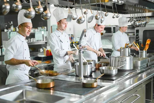 Foto de chefs de cozinha preparando algum prato dentro de uma cozinha de restaurante