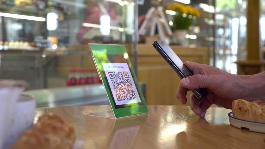 Foto de uma pessoa segurando um celular apontado para um QR Code