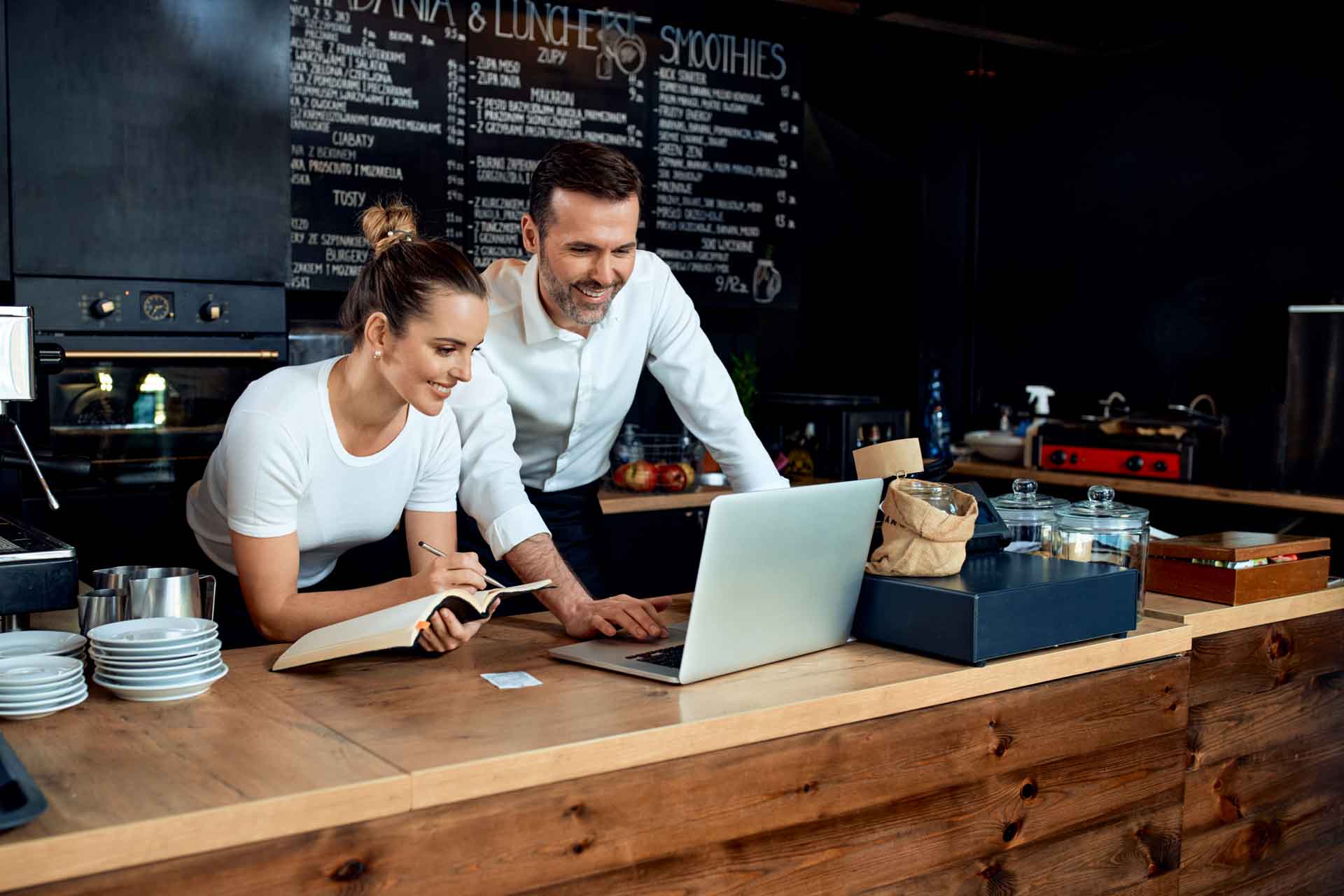 Foto de um casal olhando para um computador na bancada de um restaurante pequeno.
