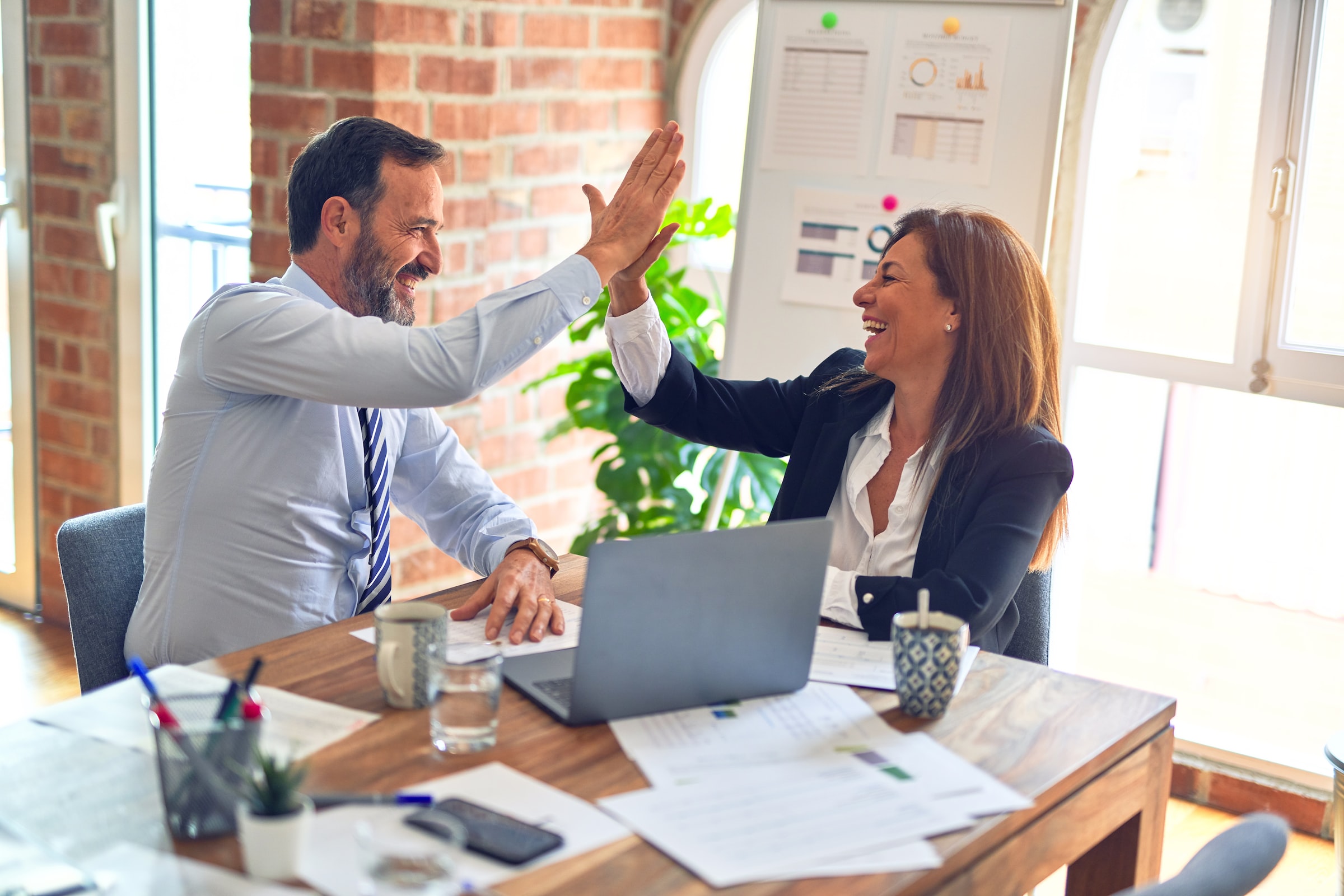 Two people in business wear high five in front of a laptop.