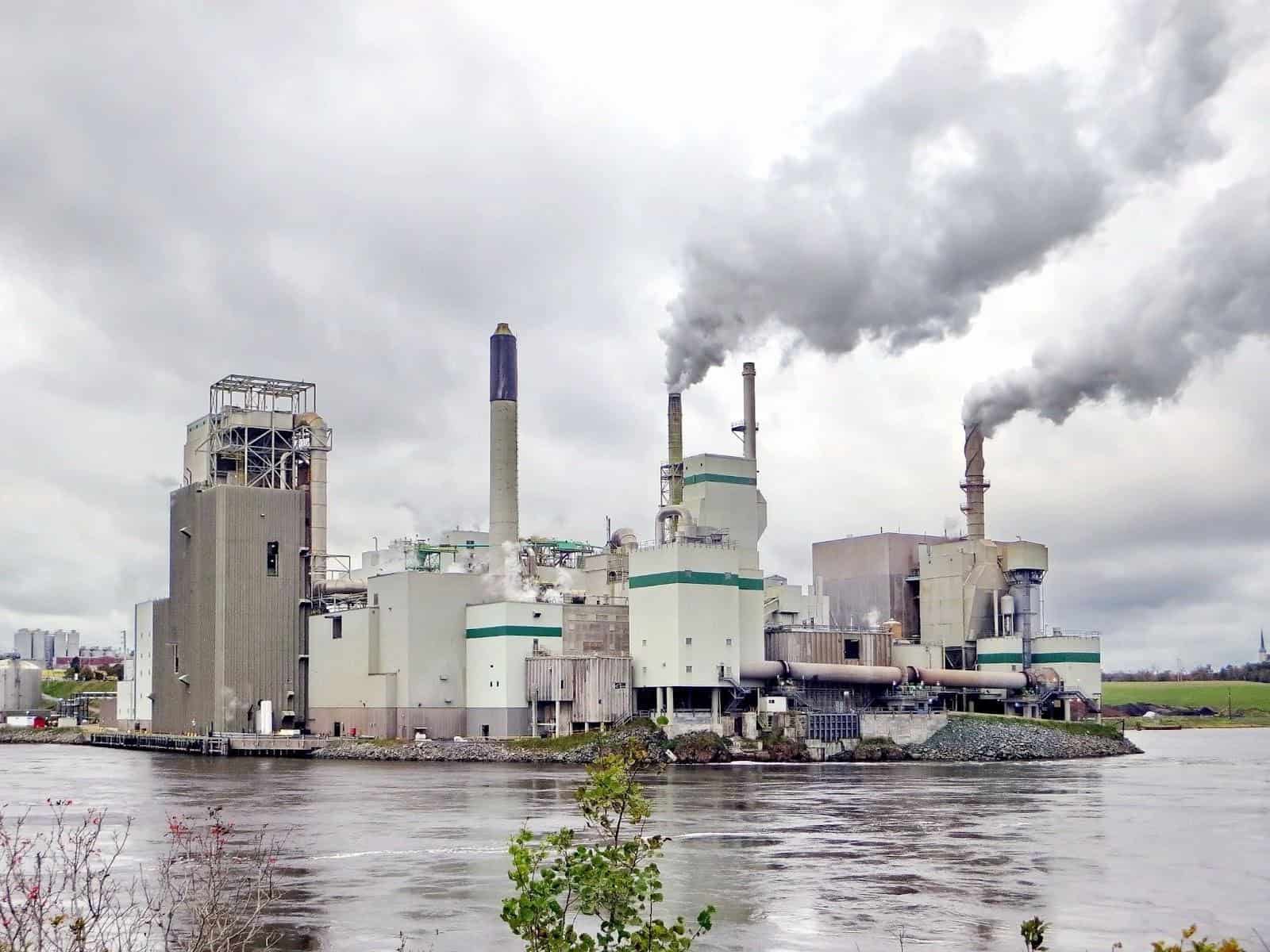 Usine au pied de l'eau qui émet d'épais nuages d'émissions.