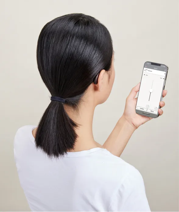 Over shoulder view of woman wearing hearing aid and looking at her phone.