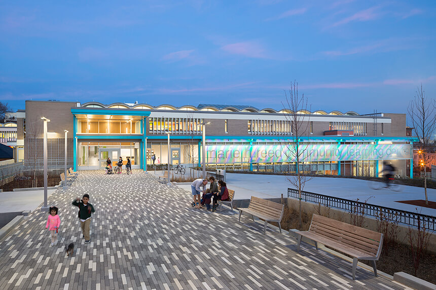 A photo of kids walking their dog near the completed Marie H. Reed Community Learning Center.