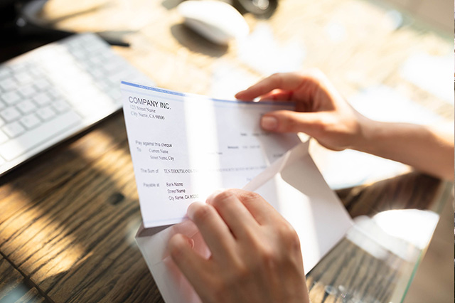 Close-up of hands putting a "Company, Inc." check into an envelope at a desk