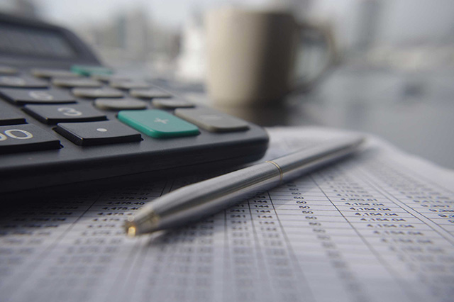 Close-up of a pen laying next to a calculator and a tan coffee cup