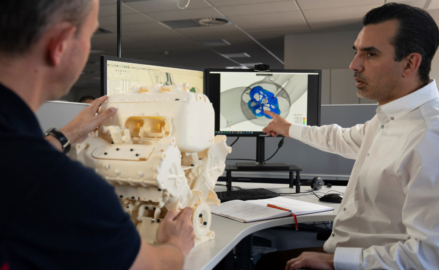 A man pointing to simulations on a computer with a physical engine prototype on the desk