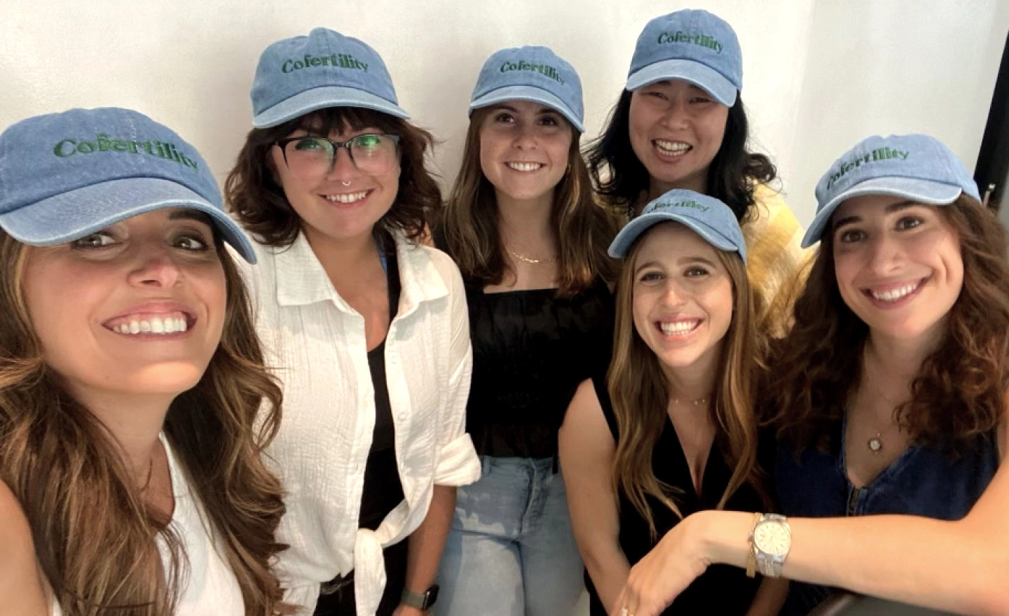 A few memers of the Cofertility team are gathered together smiling wearing Cofertility baseball hats.